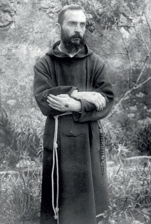 Frei Pio, aos 32 anos, de hábito capuchinho, com as mãos cruzadas no jardim do convento.