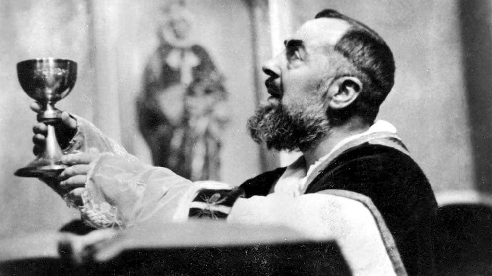 São Padre Pio, de casula, ergue o cálice na Missa, o rosto voltado para cima.