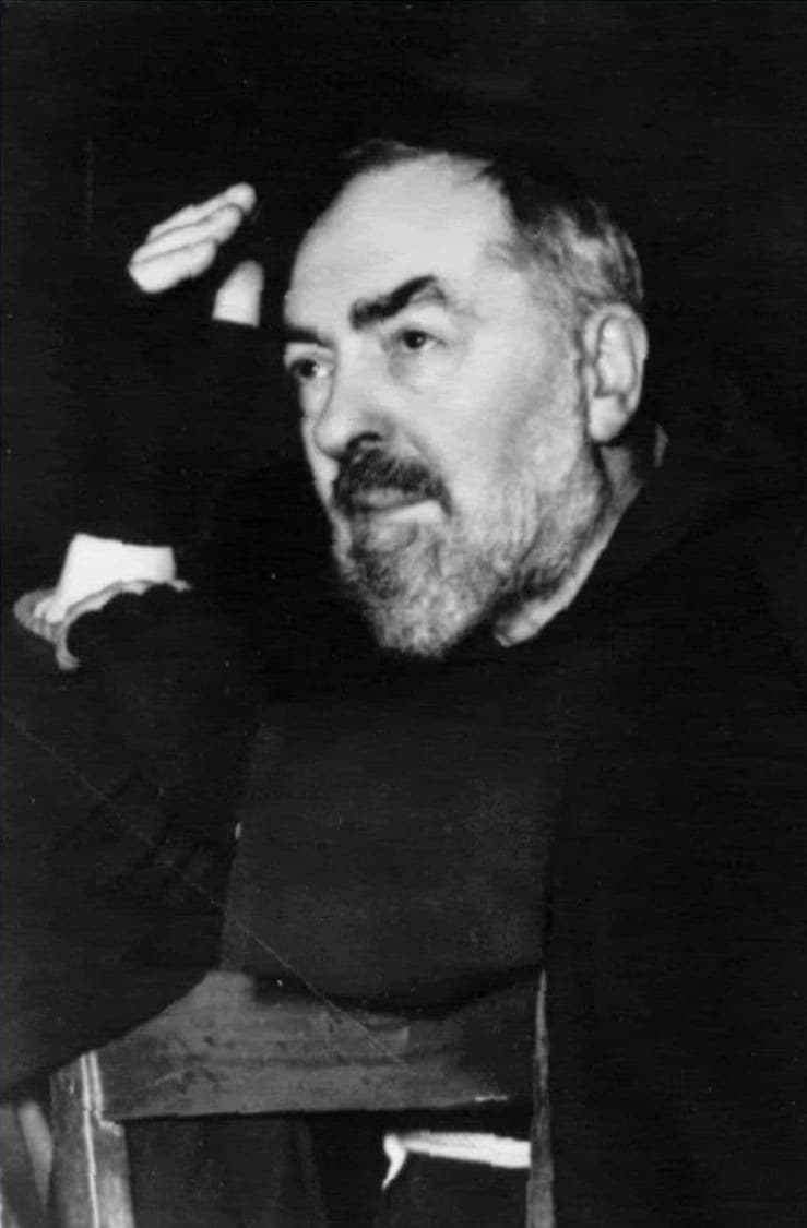 São Padre Pio de hábito capuchinho, com a mão direita erguida em bênção; a mão traz uma atadura sobre a chaga.